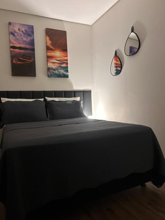 a bedroom with a black bed with three pictures on the wall at Studio 01 JD Paulistano in Ribeirão Preto