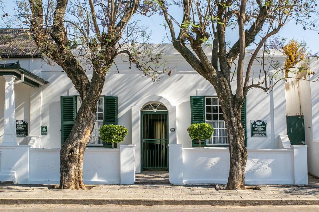 a white house with green shutters and two trees at De Kothuize 16 in Graaff-Reinet