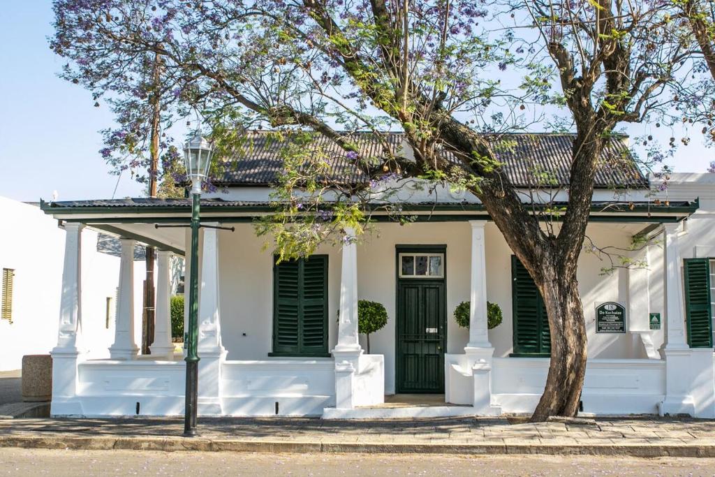 a white house with green shutters and a tree at De Kothuize 18 in Graaff-Reinet