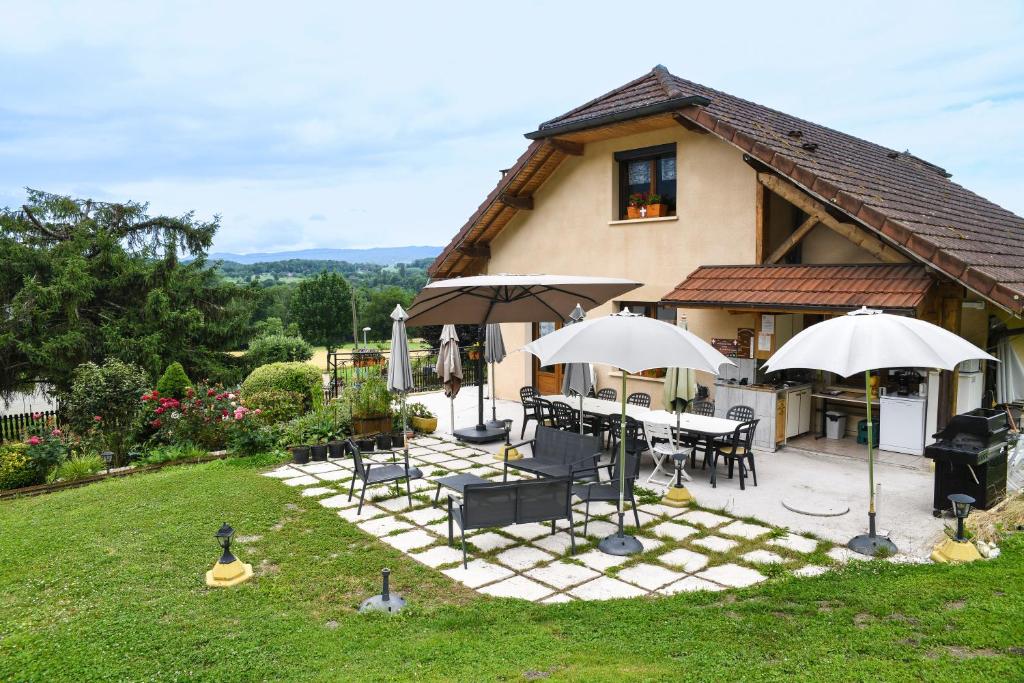 a house with tables and umbrellas in a yard at L'orée du bois in Yenne
