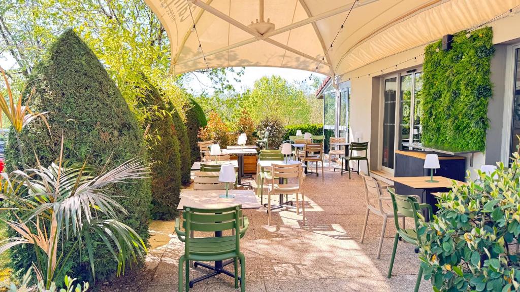 an outdoor patio with tables and chairs and plants at Campanile L'Isle d'Abeau - Bourgoin Jallieu in LʼIsle-dʼAbeau