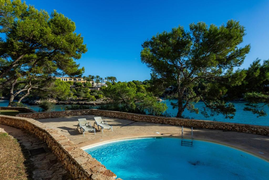 a swimming pool with two lounge chairs and trees at Ferrera Suite in Cala Ferrera