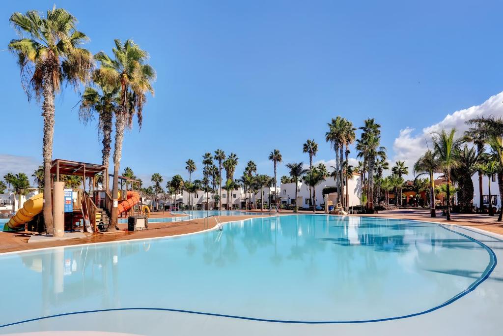 a large swimming pool at a resort with palm trees at Oasis Duna_Sun Fun Pool in Corralejo