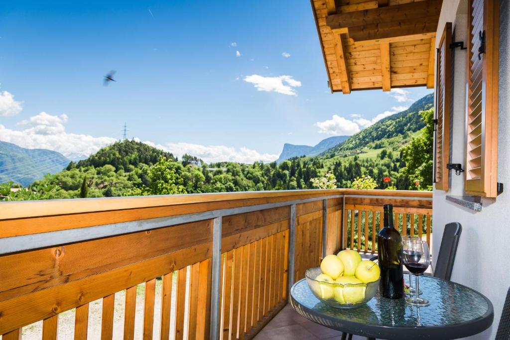 a table with a glass of wine on a balcony with mountains at Stettnerhof Wohnung Ifinger in Vollan