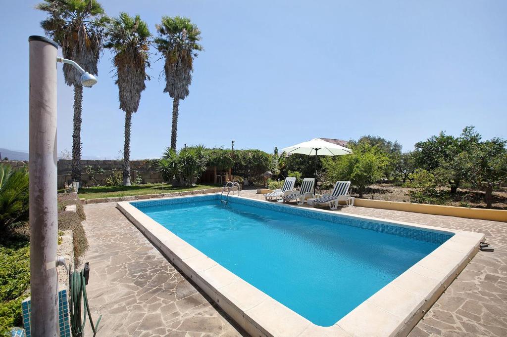 a swimming pool with palm trees and chairs and an umbrella at Las Tres Palmeras in Güimar