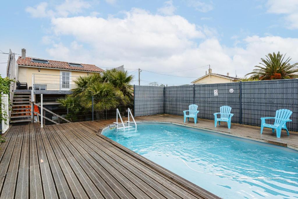 a swimming pool with two blue chairs on a wooden deck at Maison Boyardville Piscine in Saint-Georges-dʼOléron