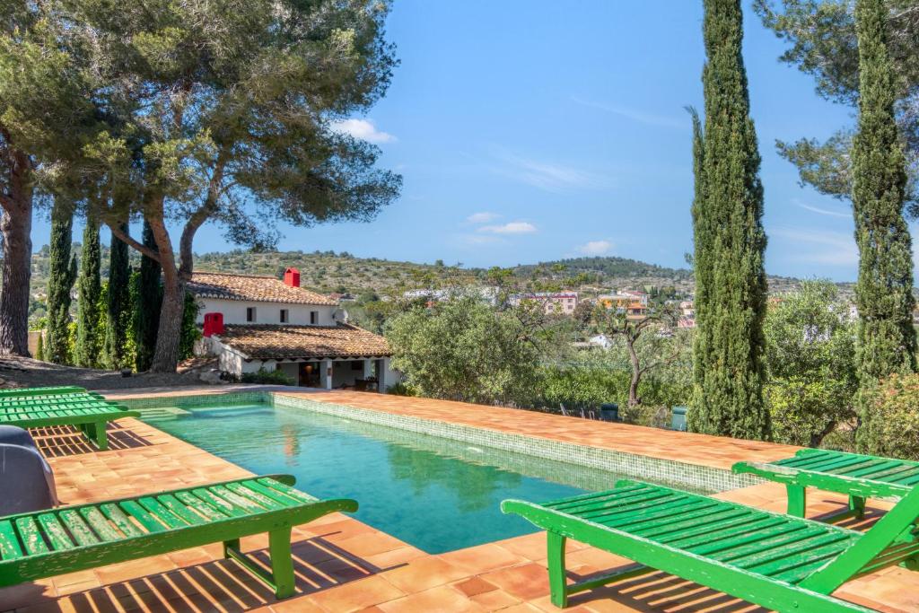 a pool with two green benches and trees at Toscana in Benissa