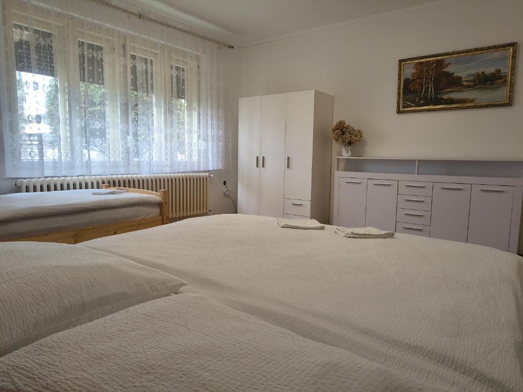 a white bedroom with two beds and a window at Vidiecky Dom in Mojmírovce