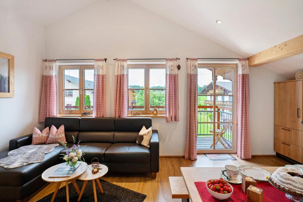 a living room with a black leather couch and windows at Neubau - Ferienwohnung Waldblick in Höslwang