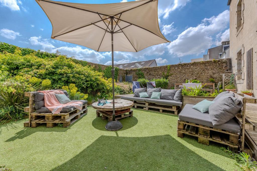 a patio with an umbrella and furniture on the grass at Maison 8 pers plein centre ville in Lesneven