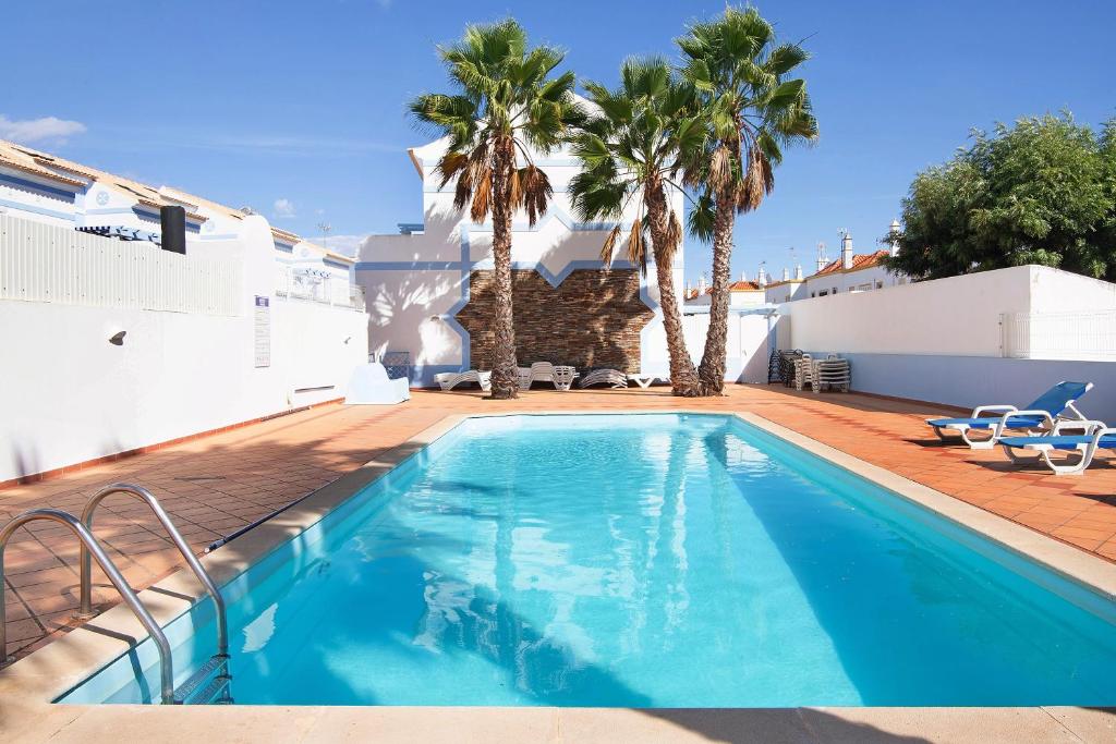 a swimming pool with palm trees and a house at Ideal Villas Residence in Vila Nova De Cacela