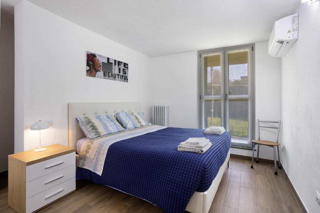 a white bedroom with a blue bed and a window at Suite Strada Persa in Pavia