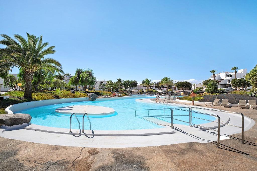 a large swimming pool in a resort with palm trees at Isla and Ocean with pool and wifi in Costa Teguise