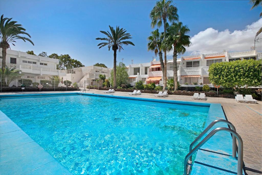 a swimming pool with palm trees and buildings at Apartamento Mertxe in Arona