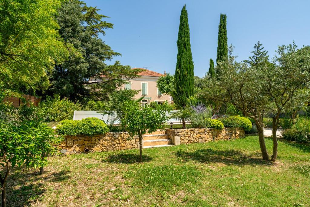 a house with a stone wall and trees at Le Secret D'hestia in Bollène