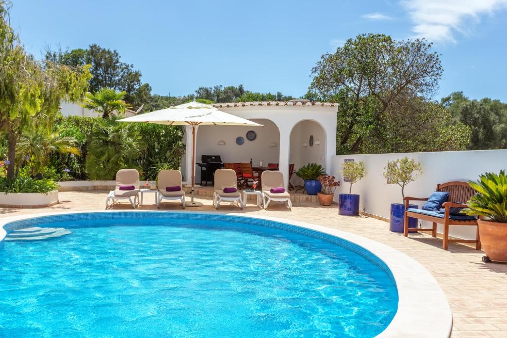 a pool with chairs and an umbrella in front of a house at Villa Sagres in Portimão