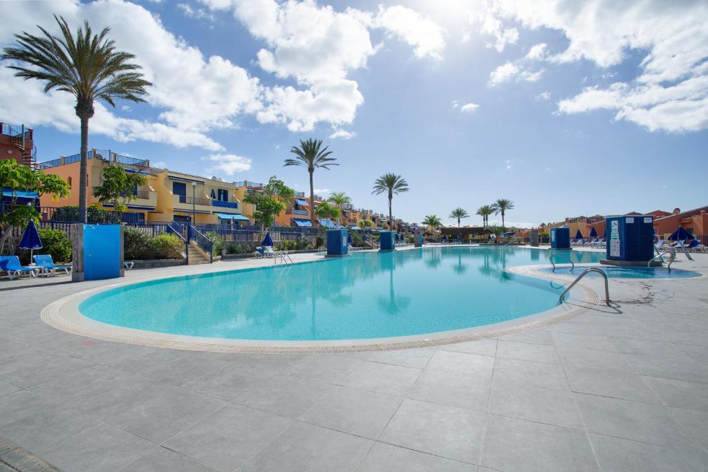 a large swimming pool with palm trees and buildings at Bahia Meloneras Luxury Duplex in Maspalomas