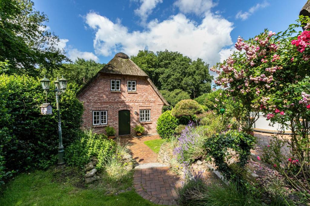an old house with a thatched roof in a garden at My Little Rose Cottage in Dörpling
