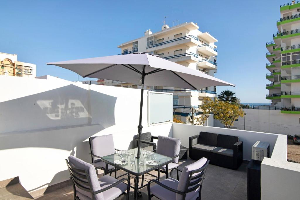 a table and chairs with an umbrella on a balcony at Telmus Villa 1 andar in Monte Gordo