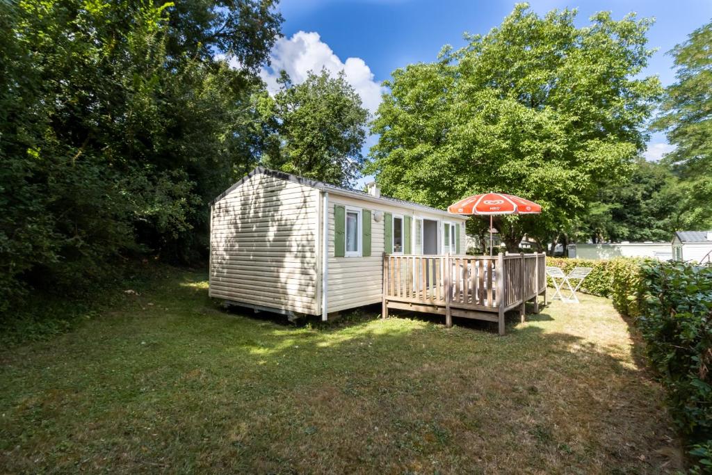 a tiny house with an umbrella and a deck at Mobilhome Le Chataignier in Saint-Pompont