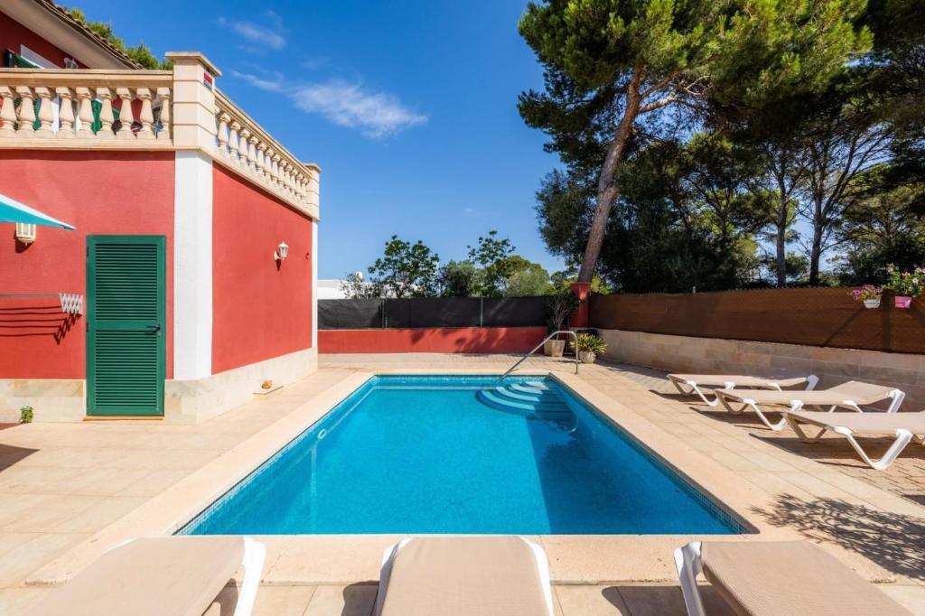 a swimming pool next to a red house with chairs at Villa Malena in Llucmajor
