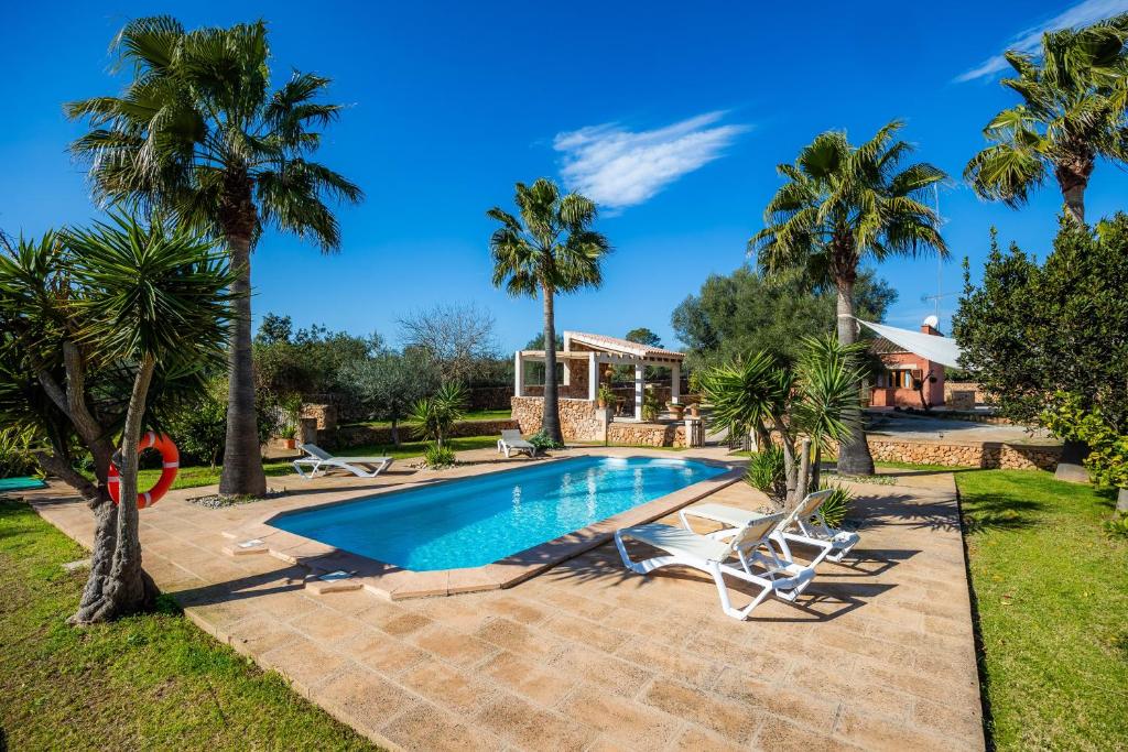 a swimming pool with palm trees in front of a house at Finca Ca S'Hereu Mas in Campos