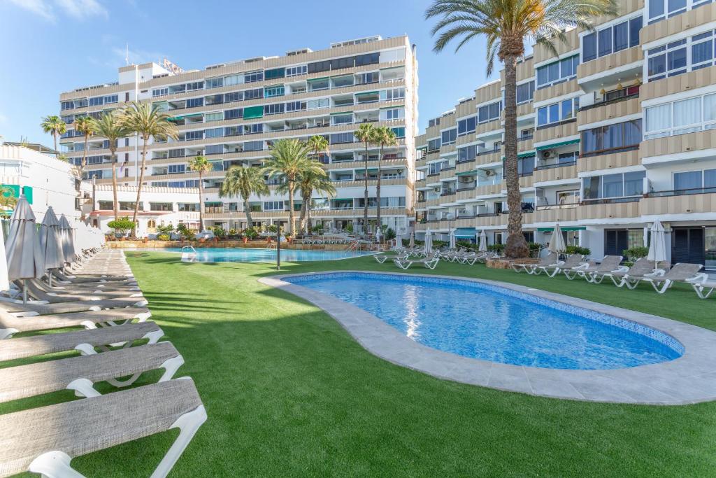 a resort with a pool and chairs and a building at Estudio Yumbo Playa in San Bartolomé
