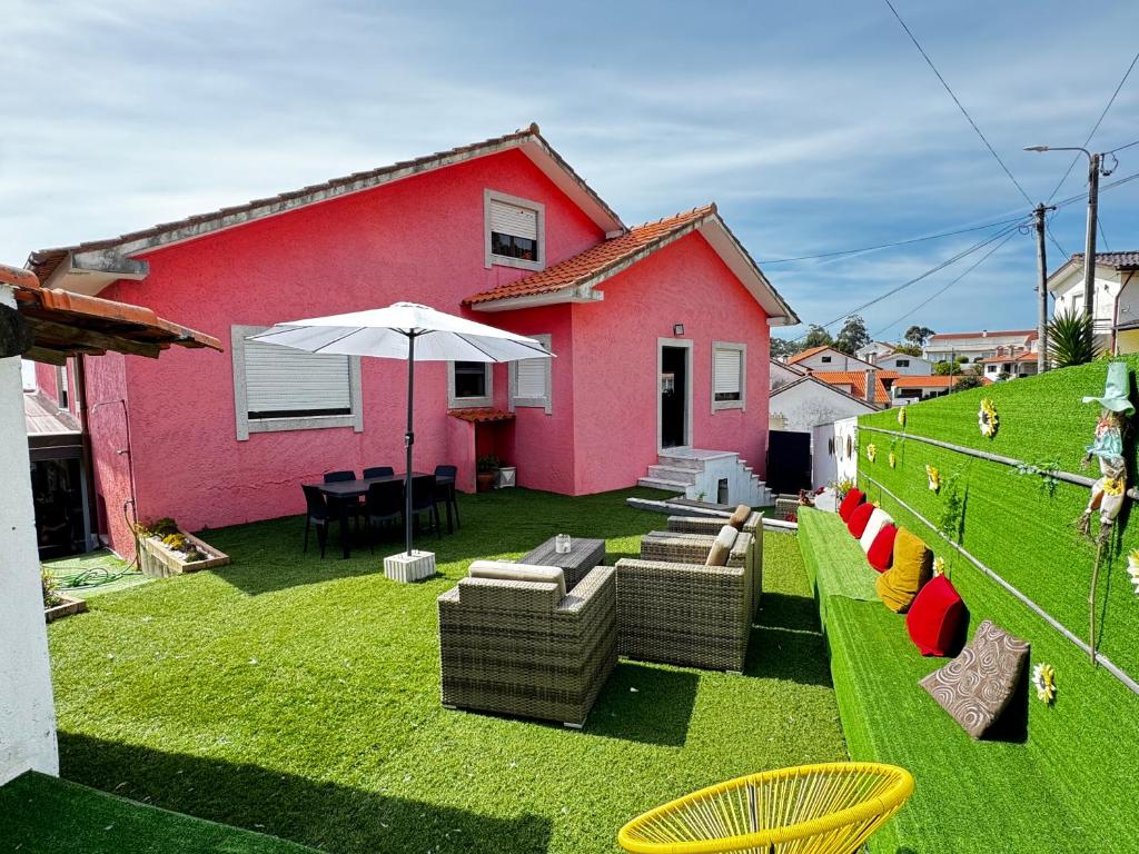 a pink house with chairs and an umbrella on a yard at Refugio Senhora Paz in Marinhas