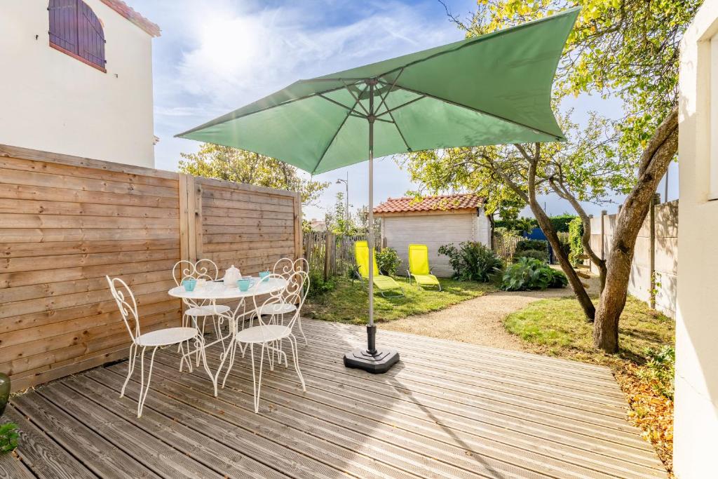a table and chairs on a wooden deck with a green umbrella at Bois Flottés - Maisonnette 700m mer in Pornic