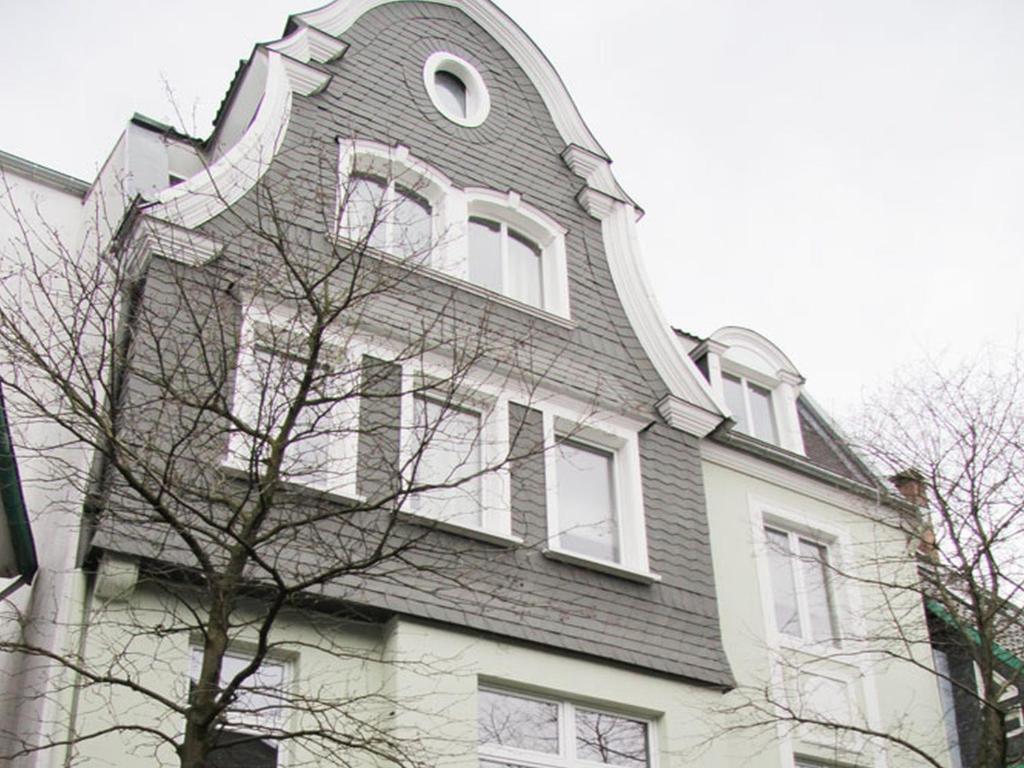 a building with a gambrel roof and a tree at Serviced Apartments Xanthurus in Schwelm