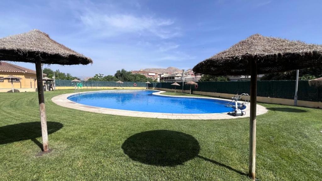 a swimming pool with two umbrellas on the grass at Ágora Alhambra in Atarfe