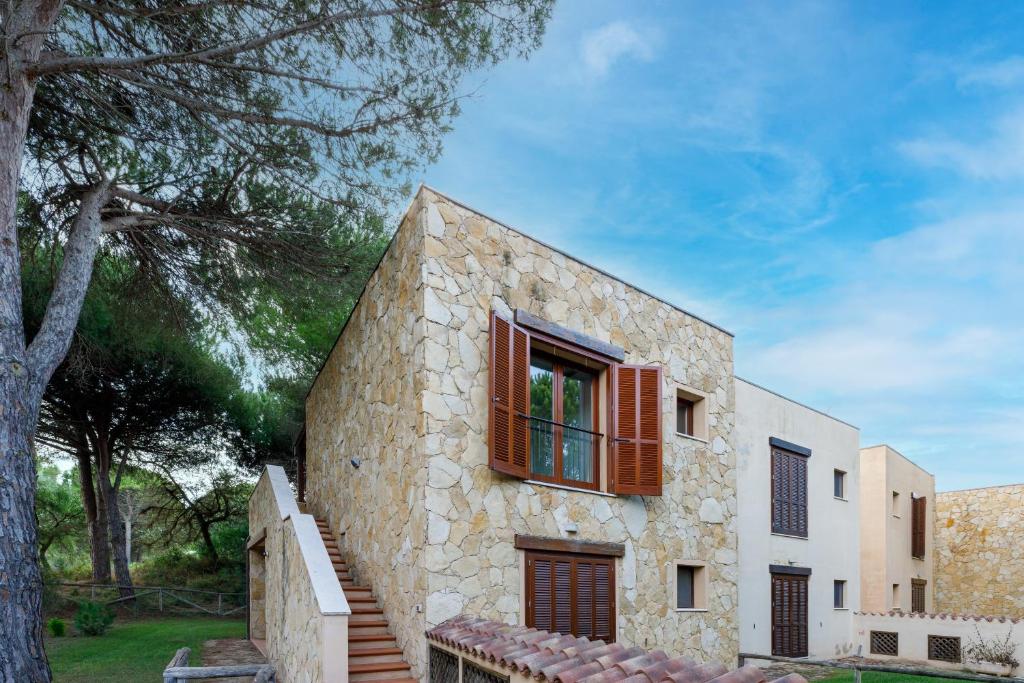a stone house with red windows and a tree at Casa Antonella sul Golf in S'archittu Cuglieri
