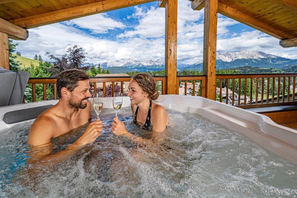a man and woman holding glasses of wine in a hot tub at Chalet Schlossberg Schlern in Nova Ponente