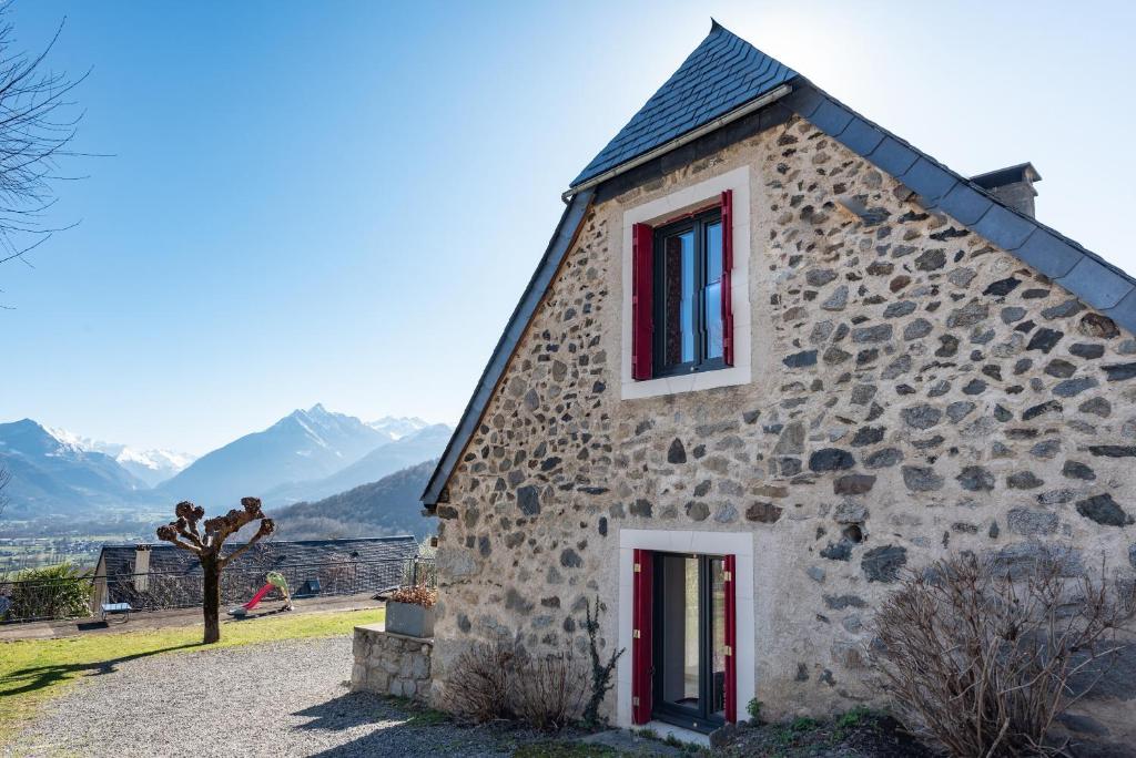 a stone house with red windows and mountains in the background at Gite d'Ayzi in Ouzous