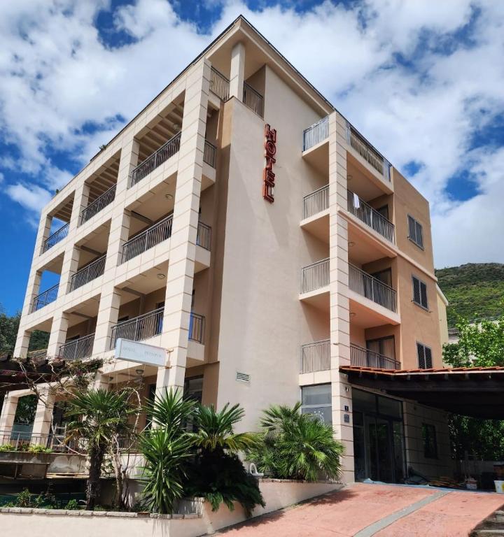 a large white building with palm trees in front of it at Hotel Petrovac in Petrovac na Moru