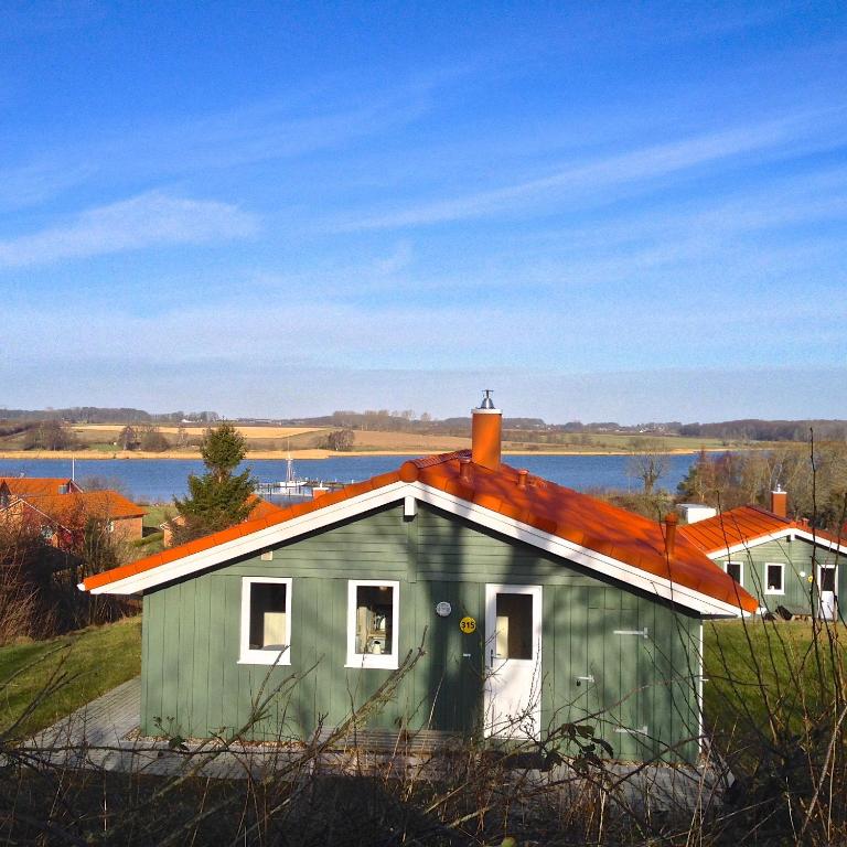 a green house with an orange roof next to a lake at Skipper-Lodge Süd in Kosel