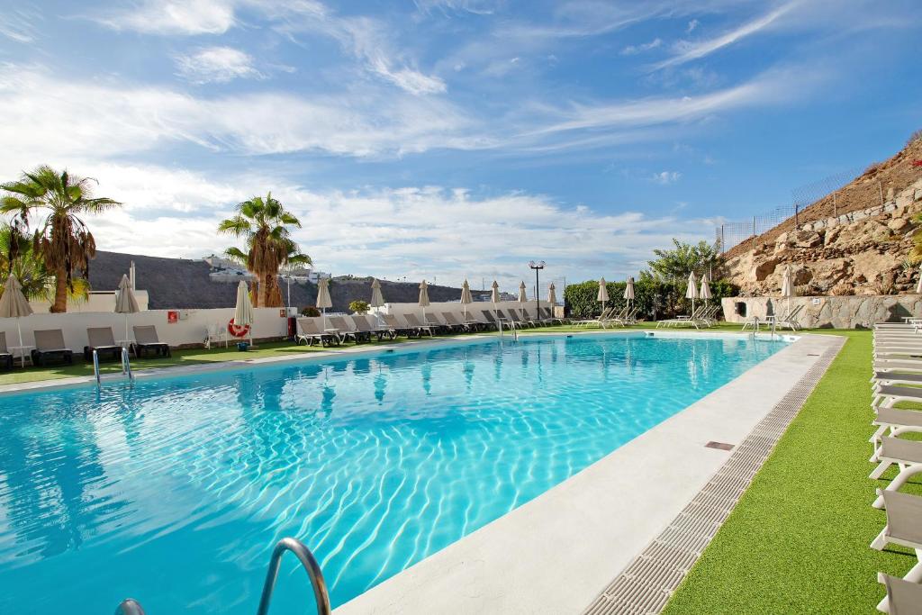 a large swimming pool with chairs and palm trees at Zen House in Puerto Rico de Gran Canaria