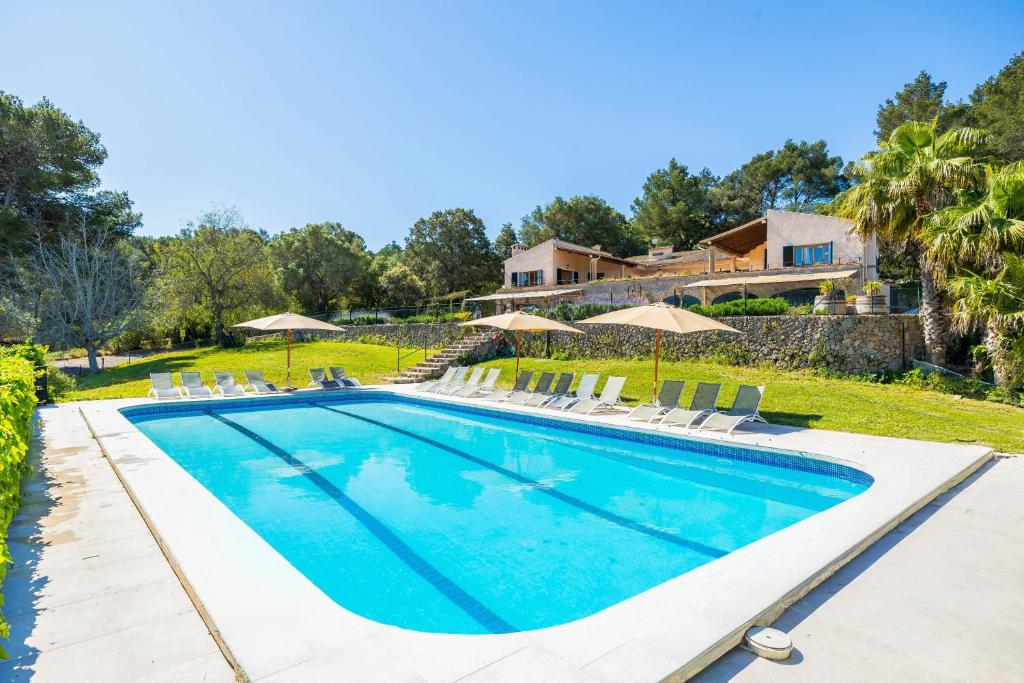 a pool with chairs and umbrellas in front of a house at Es Puig de Ses Coves in Santa Eugenia