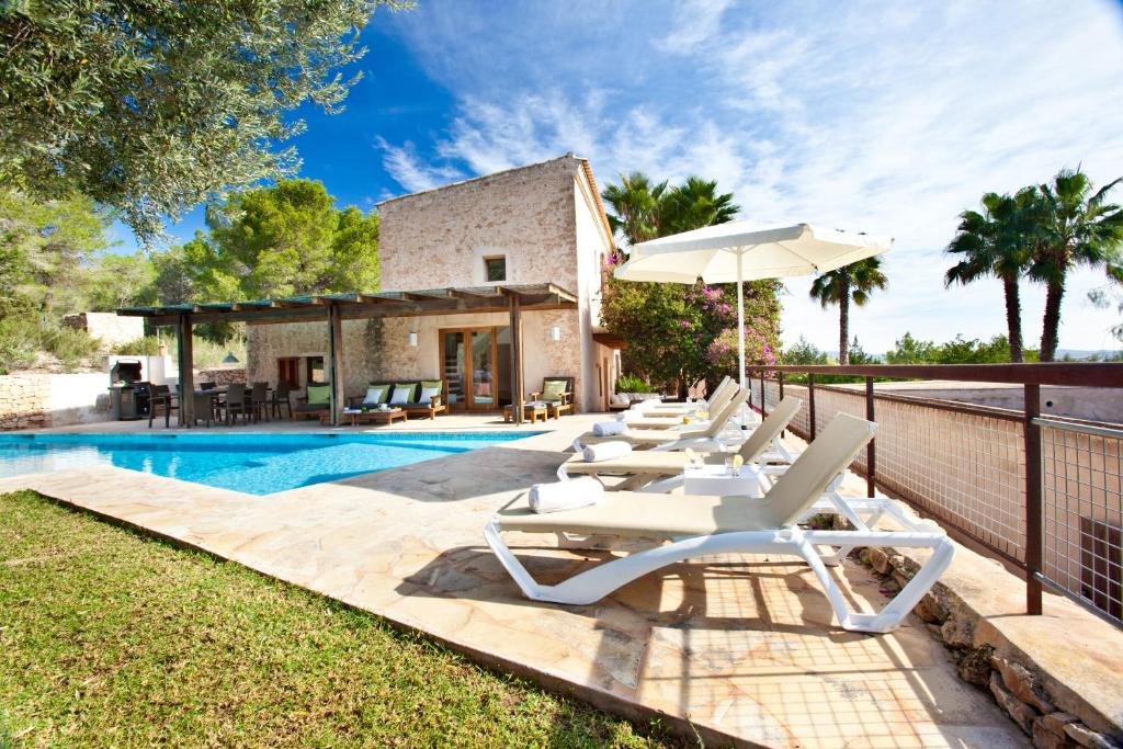 a pool with lounge chairs and an umbrella next to a house at Villa Can Rafal Ibiza in Sant Josep de sa Talaia