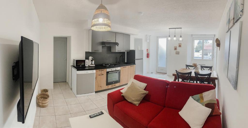a living room with a red couch and a kitchen at Gîte bord de mer - le Chardon in Pirou
