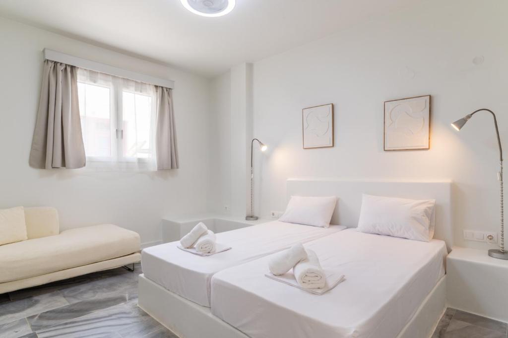 a white bedroom with two beds and a couch at A Tinian Room 2 in Tinos