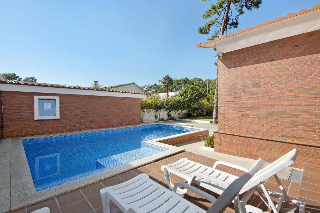 a swimming pool with white chairs next to a brick building at Moradia Pinheiro Manso in Apúlia