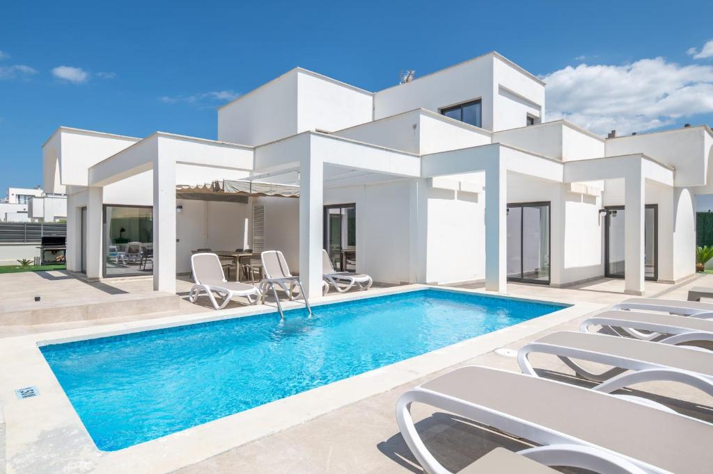 a white house with a swimming pool and chairs at Villa Sam 3 in Can Picafort