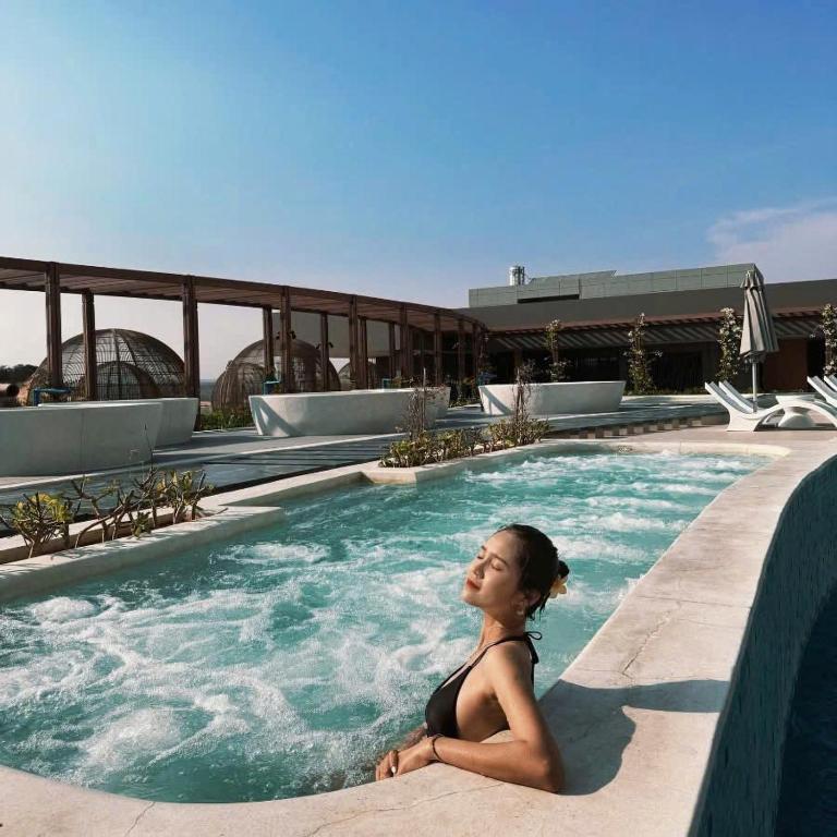 a woman sitting in a swimming pool at Apec Beach Luxury Mũi Né in Mui Ne