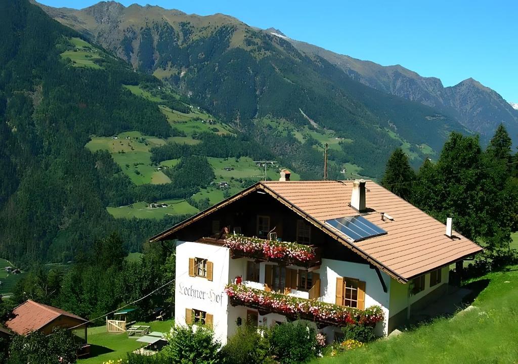 a house on a hill with mountains in the background at Lechnerhof Appartement Alpenrose in Schenna