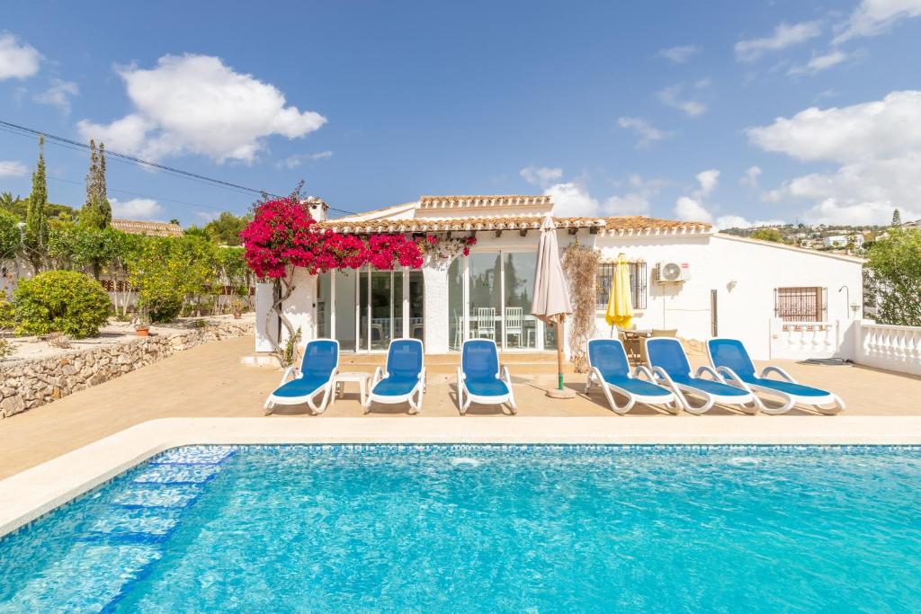a swimming pool with blue chairs and a house at Villa Andes in Benissa