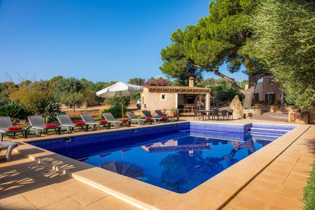 a pool with chairs and an umbrella next to a house at Ses Angoixes in Santanyi
