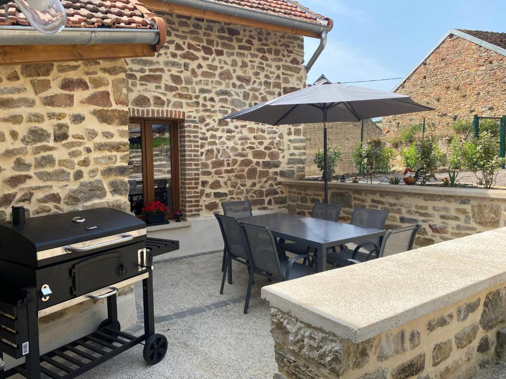 a patio with a grill and a table with chairs and an umbrella at La petite Cocotte in Marcheseuil