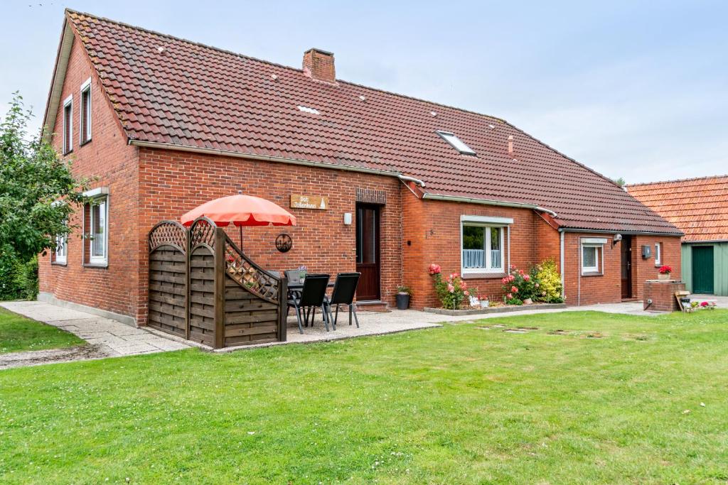 a house with a table and chairs and an umbrella at Dat Jollenhuus in Ihlow