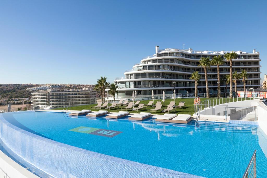 a large swimming pool with lounge chairs and a large building at Infinity View by Mar Holidays - Arenales del Sol in Arenales del Sol